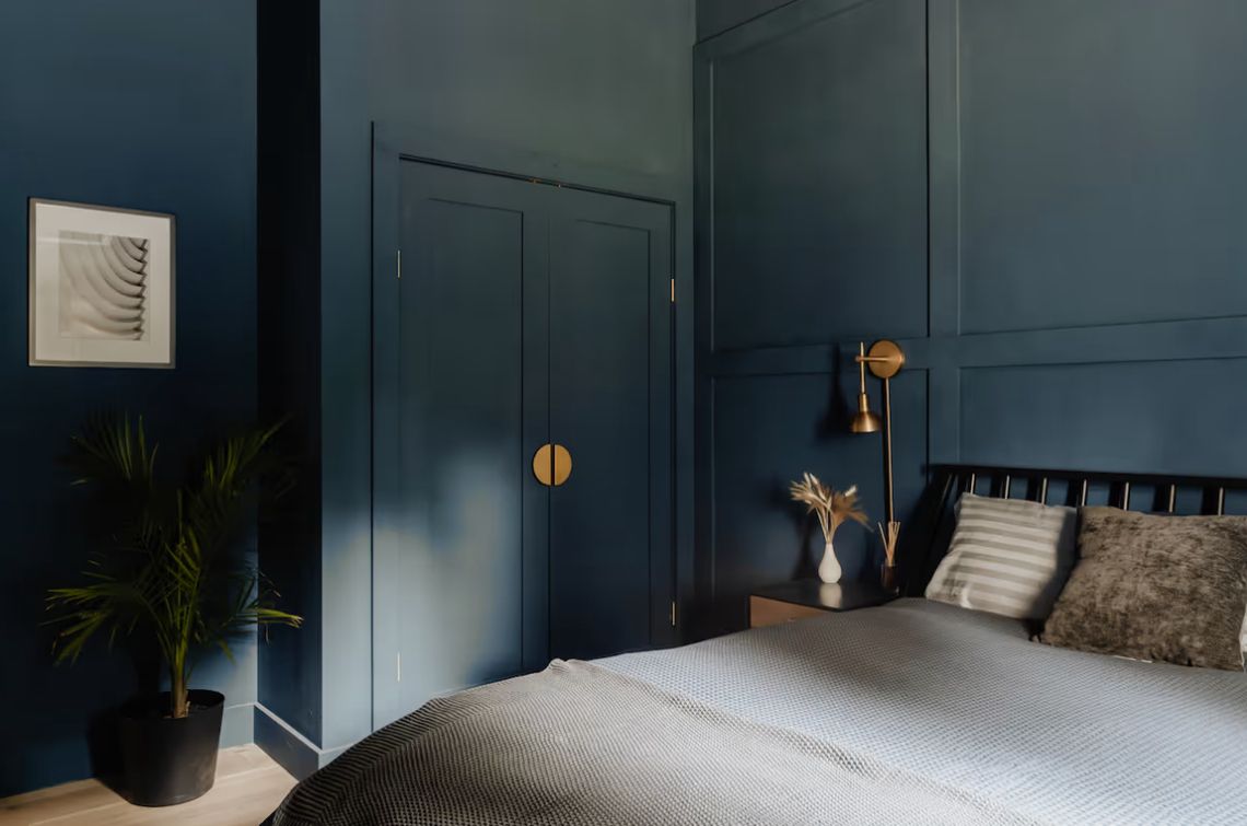 Navy bedroom with paneled walls and brass hardware